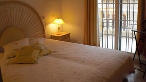 Une chambre d’hôtel avec un lit, une table de chevet avec une lampe, une fenêtre avec des barreaux et une chaise.