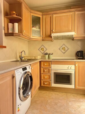 A kitchen with wooden cabinets, a washing machine, an oven, and a countertop with a kettle.