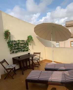 Une terrasse extérieure avec une table, des chaises, un coin salon avec des coussins et un parasol.