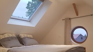 A bedroom with a skylight, a round window, and a bed with a headboard.