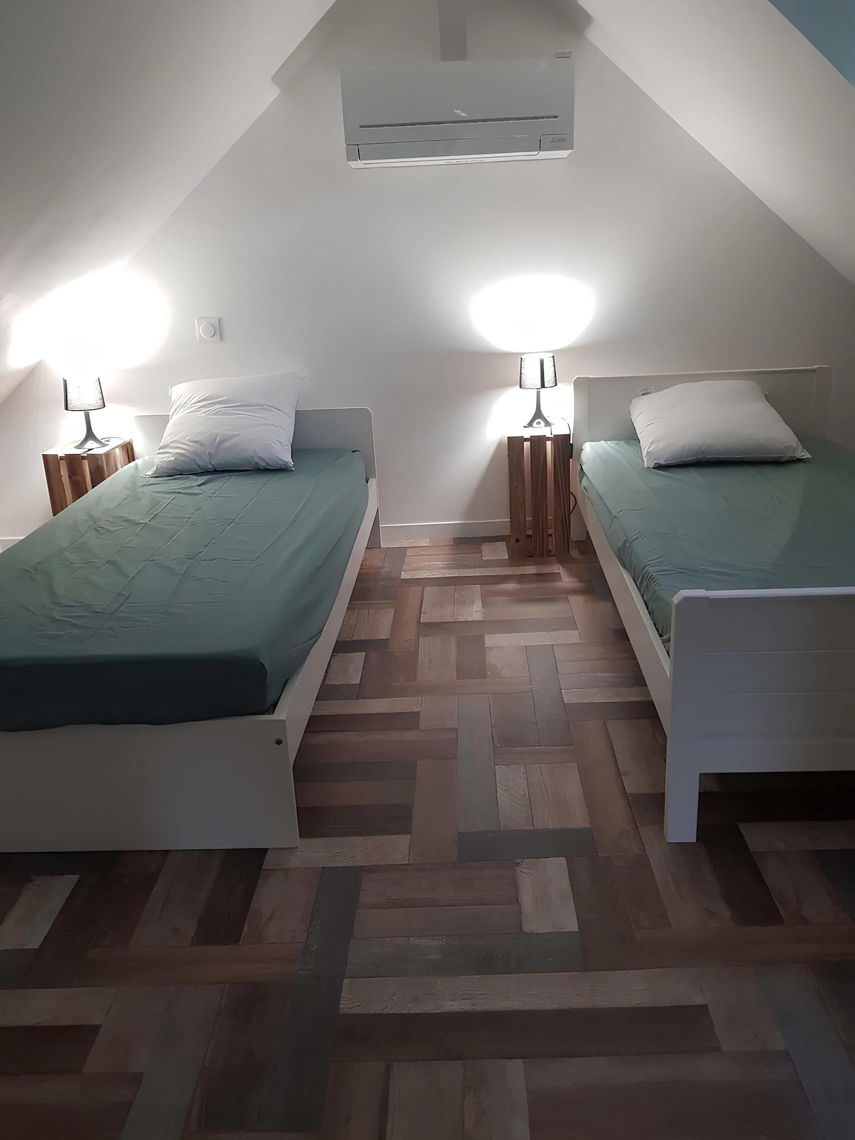 Un dormitorio con dos camas, piso de madera con diseño espiga y ventilador de techo.