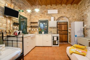 A compact room with a kitchenette, a bed, a TV, and a stone wall.