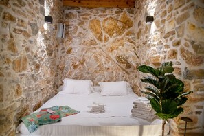 A stone-walled room with a bed, pillows, a plant, and a wall-mounted air conditioner.