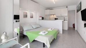 A modern hotel room with a bed, a green bedspread, a small kitchenette, and a flat-screen TV. - Vacation Studio 'Loft Guanapay 1' with Private Terrace, Wi-Fi, and Air Conditioning (Arona)