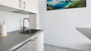 A modern kitchen with a stainless steel sink, white cabinets, and a scenic coastal painting on the wall. - Vacation Studio 'Loft Guanapay 1' with Private Terrace, Wi-Fi, and Air Conditioning (Arona)
