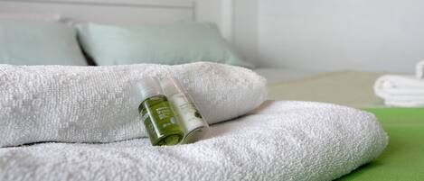 A neatly made bed with white and green linens, a bottle of body lotion, and a pillow.
