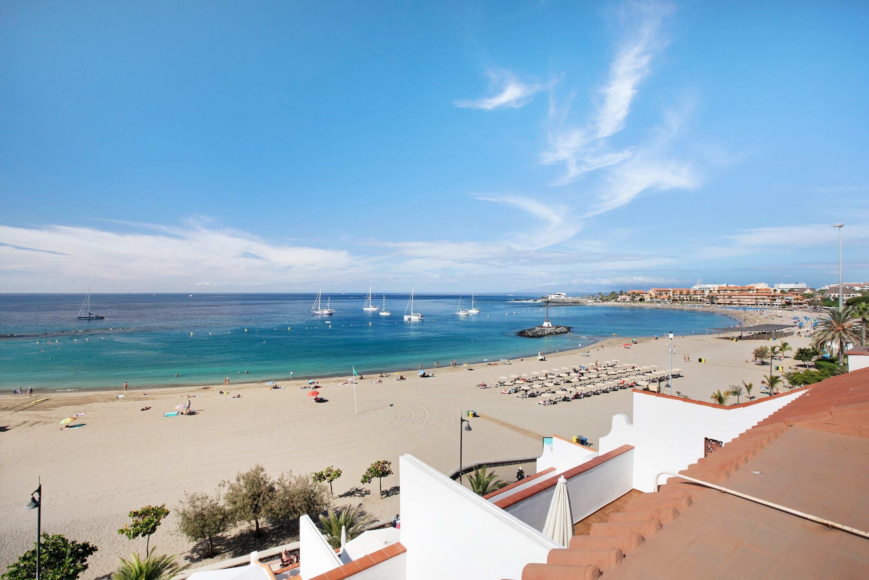A coastal beach scene with boats, a sandy beach, and a town in the background.