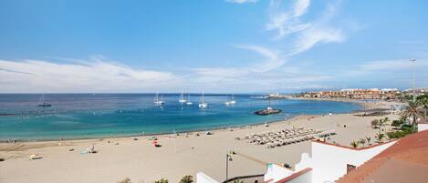 A coastal beach scene with boats, a sandy beach, and a town in the background.