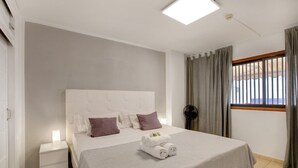 A modern hotel room with a large bed, a bedside table, a nightstand, a window with curtains, and a ceiling light. - Vacation Apartment 'Las Fuentes' with Sea View, Private Terrace and Wi-Fi (Arona)