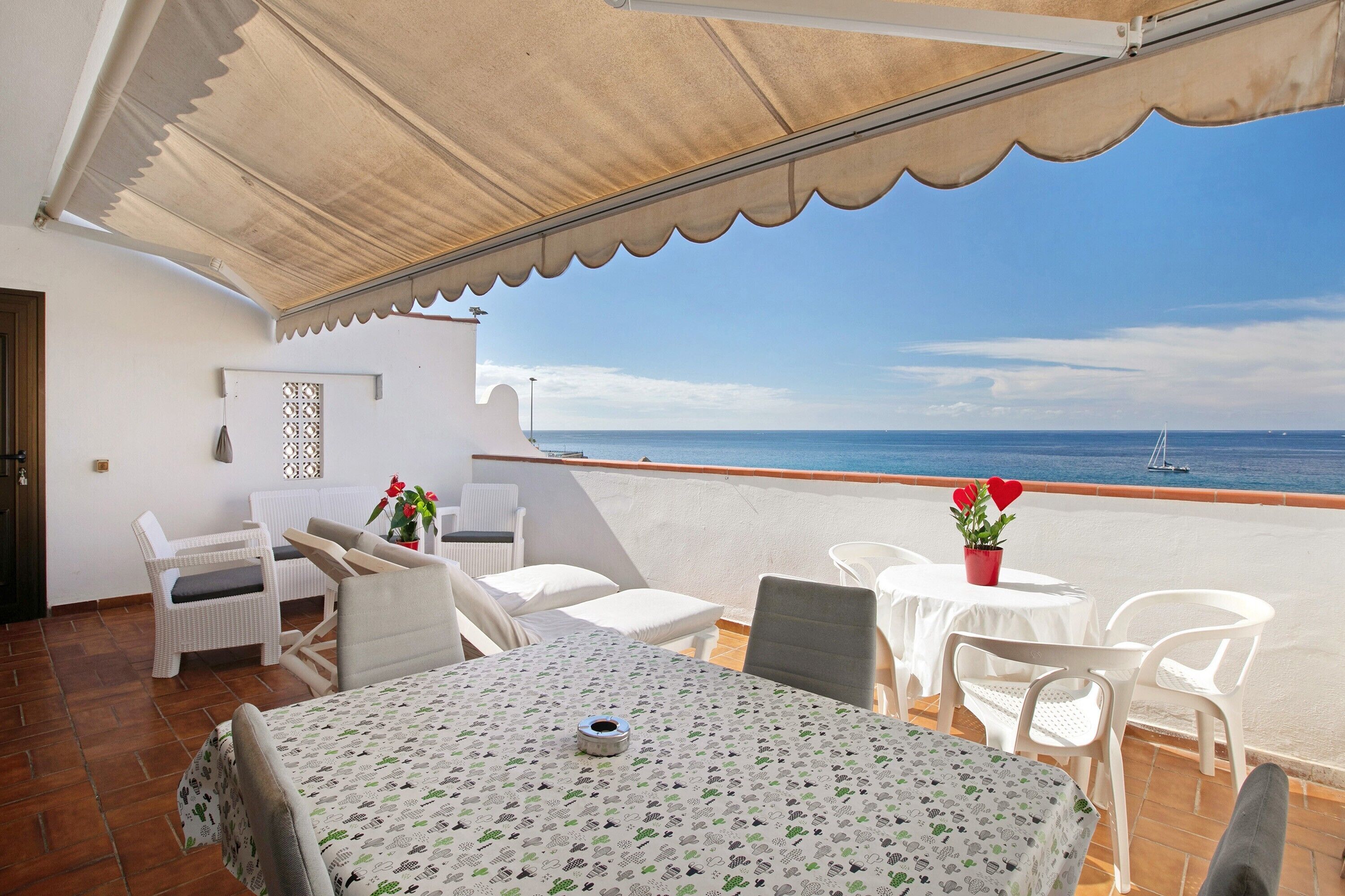 A terrace with a table, chairs, and a view of the sea.