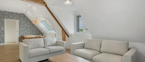 Una sala de estar moderna estilo loft con techo alto, vigas de madera a la vista, un comedor y tragaluces.