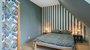 Un dormitorio con una cama, dos lámparas de noche, una pared a rayas y una cortina estampada.
