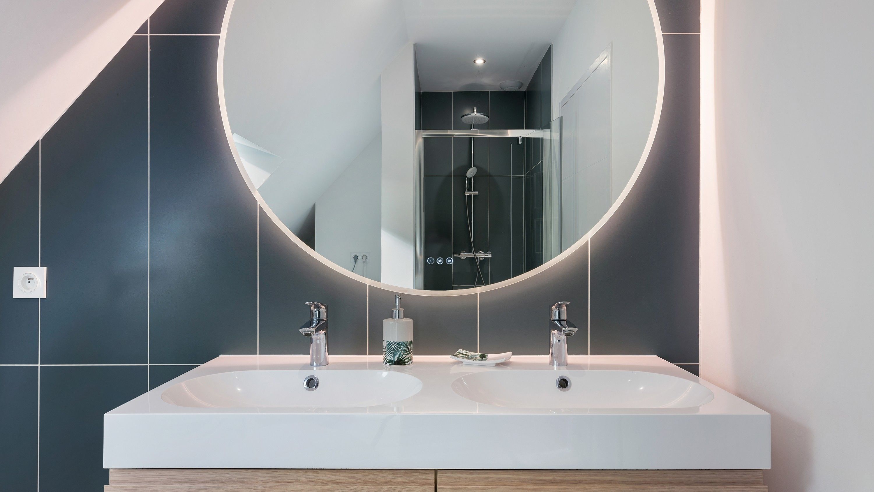 A modern bathroom with a large mirror, two sinks, and a shower.