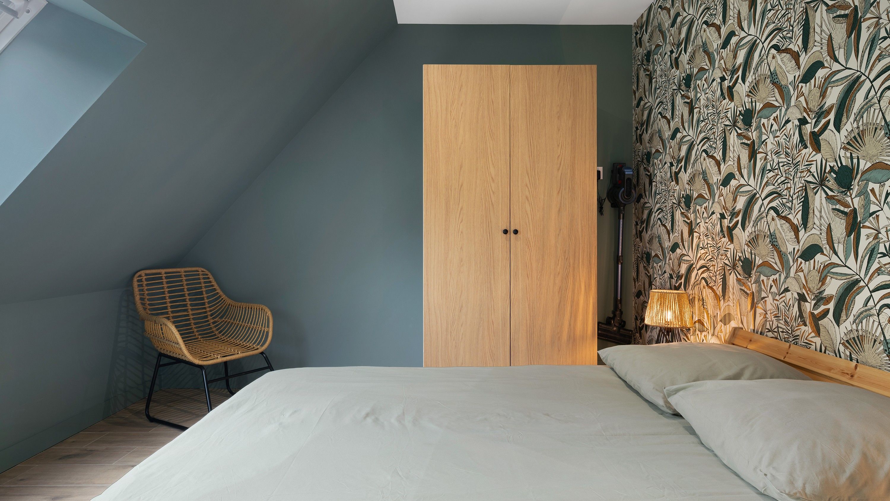 A bedroom with a bed, a chair, a wardrobe, and a patterned wallpaper.
