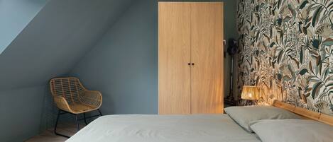 A bedroom with a bed, a chair, a wardrobe, and a patterned wallpaper.
