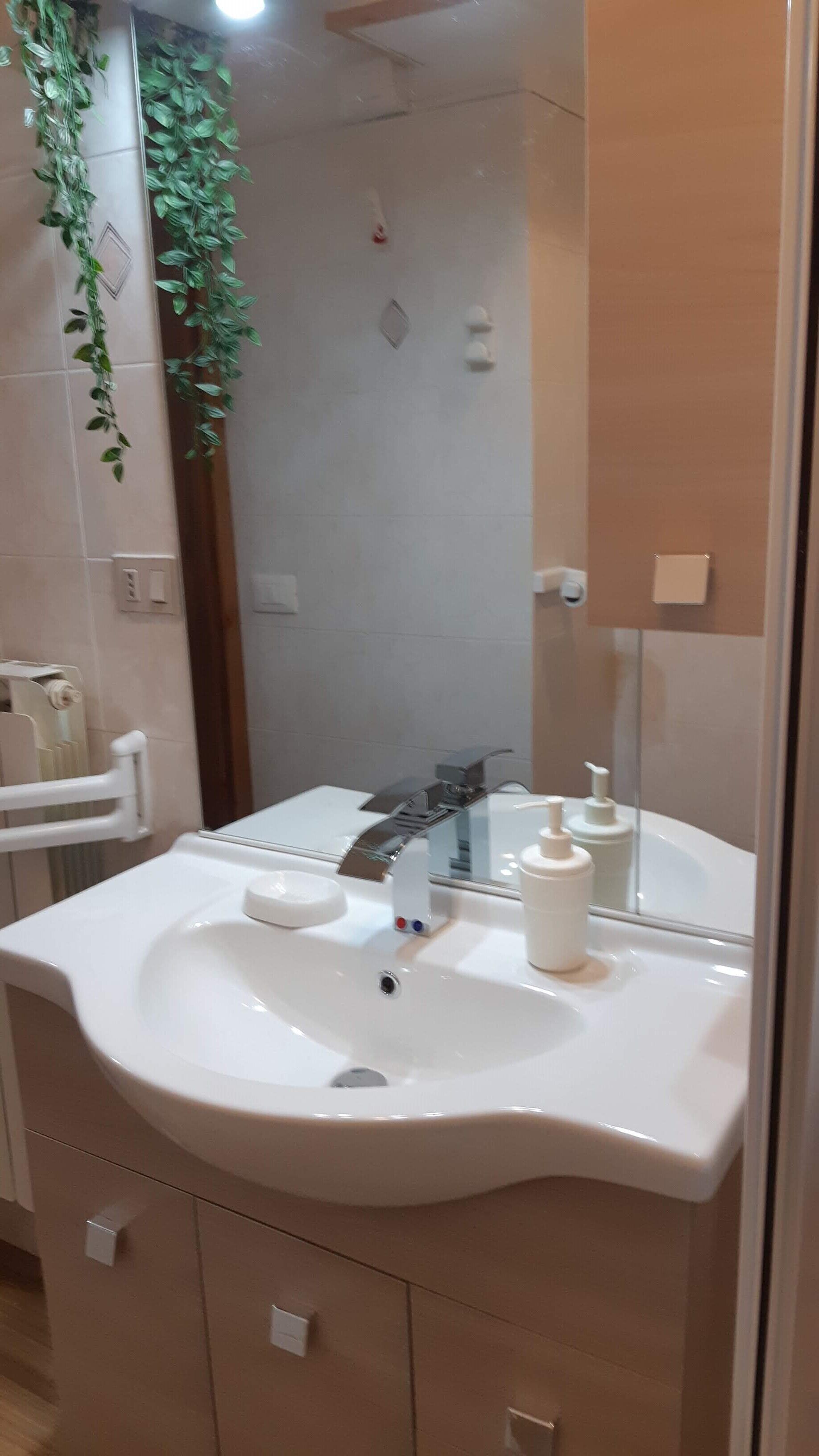 Un baño con lavamanos blanco, un espejo, grifo, dispensador de jabón y radiador.