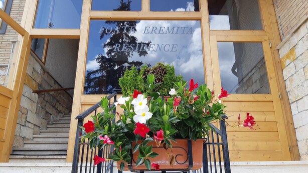 Un bâtiment en bois avec une enseigne indiquant « FONTE EREMITA RESIDENCE » et un pot de fleurs placé devant l’entrée.