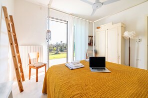 Una camera da letto con un letto, un computer portatile, una sedia, una scala di legno e vista sull'esterno.