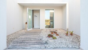 Une entrée moderne avec une porte en verre, un chemin en pierre et des plantes en pot.