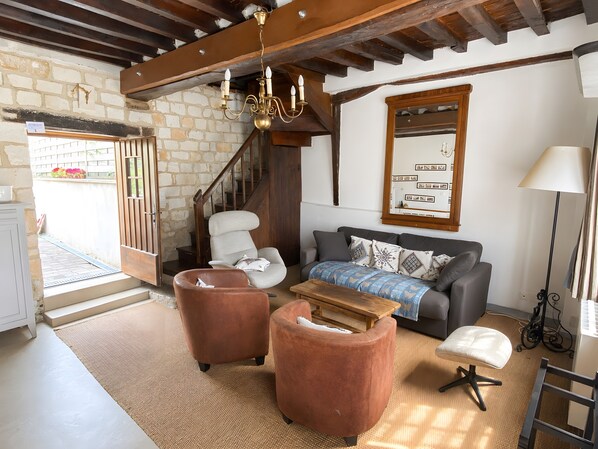 A living room with a sofa, two armchairs, a wooden coffee table, a chandelier, a staircase, and a mirror on the wall.