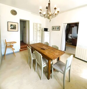 A dining area with a wooden table, white chairs, a chandelier, and a white cabinet with a microwave.