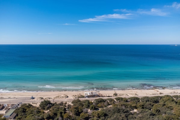A coastal view with a beach, a small building, and a road leading to the beach.