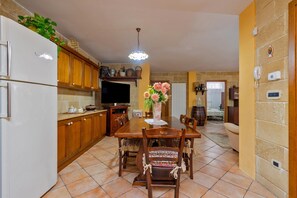 A kitchen with wooden cabinets, a dining table with chairs, a refrigerator, and a vase with flowers.