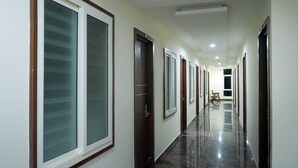A long, narrow hallway with doors on both sides, a chair in the middle, and a polished floor. - HOTEL NIVETHA INN (Coimbatore)
