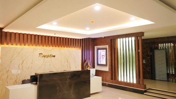 A reception area with a marble wall, a reception desk, and a modern ceiling design. - HOTEL NIVETHA INN (Coimbatore)