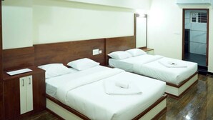 A hotel room with two beds, wooden headboards, a wardrobe, and a bathroom with a tiled floor. - HOTEL NIVETHA INN (Coimbatore)
