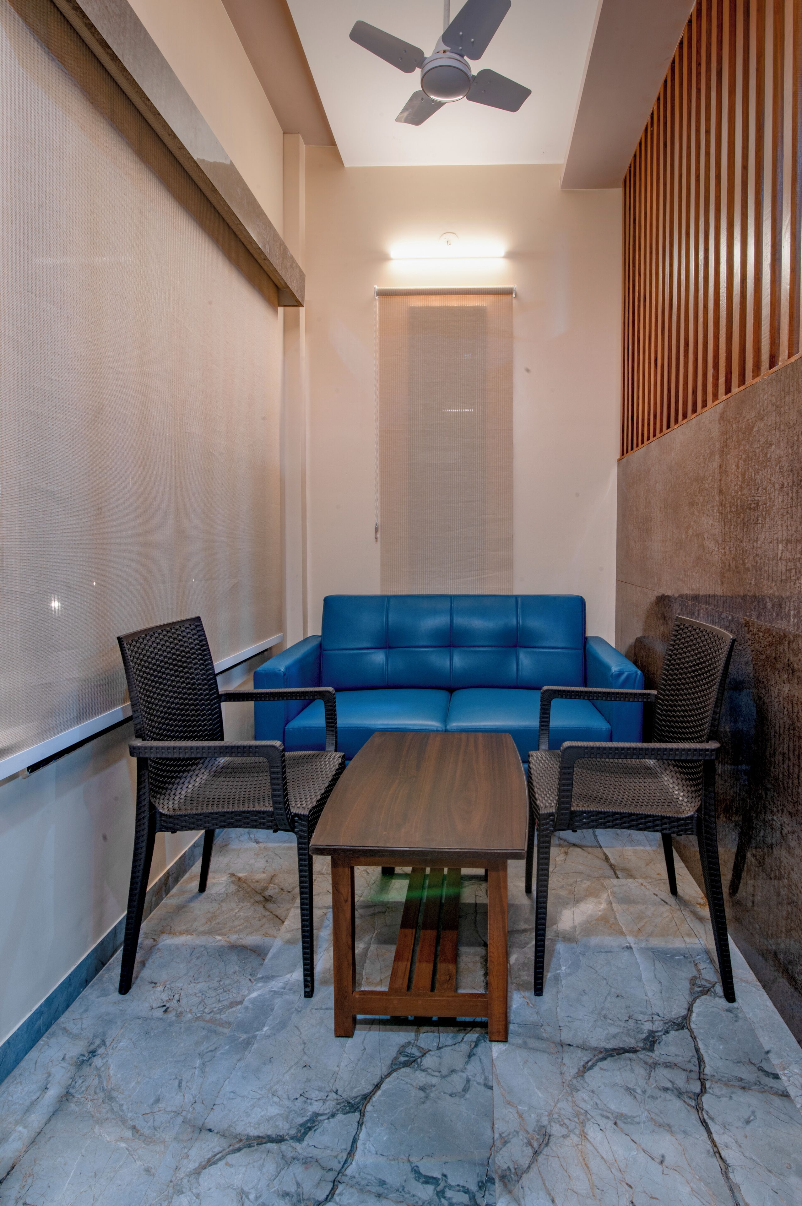 A modern interior with a blue sofa, two wicker chairs, a wooden coffee table, and a ceiling fan.