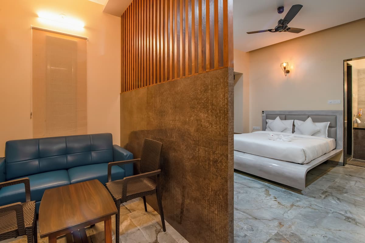 A hotel room with a blue sofa, a wooden accent wall, a bed with white bedding, and a ceiling fan.