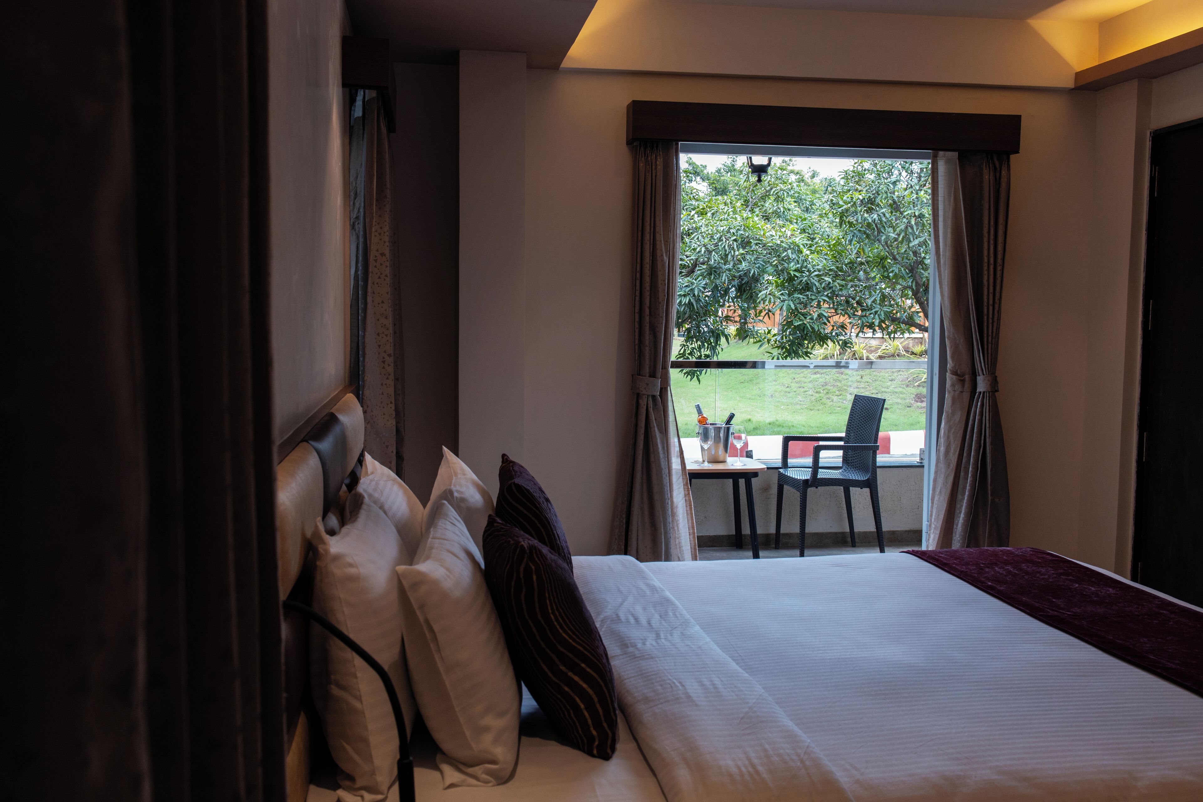 A hotel room with a large bed, a view of the outdoors, and a table with chairs outside the window.