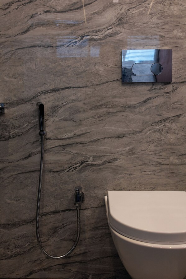 A bathroom with a marble floor, a shower with a handheld hose, and a toilet.
