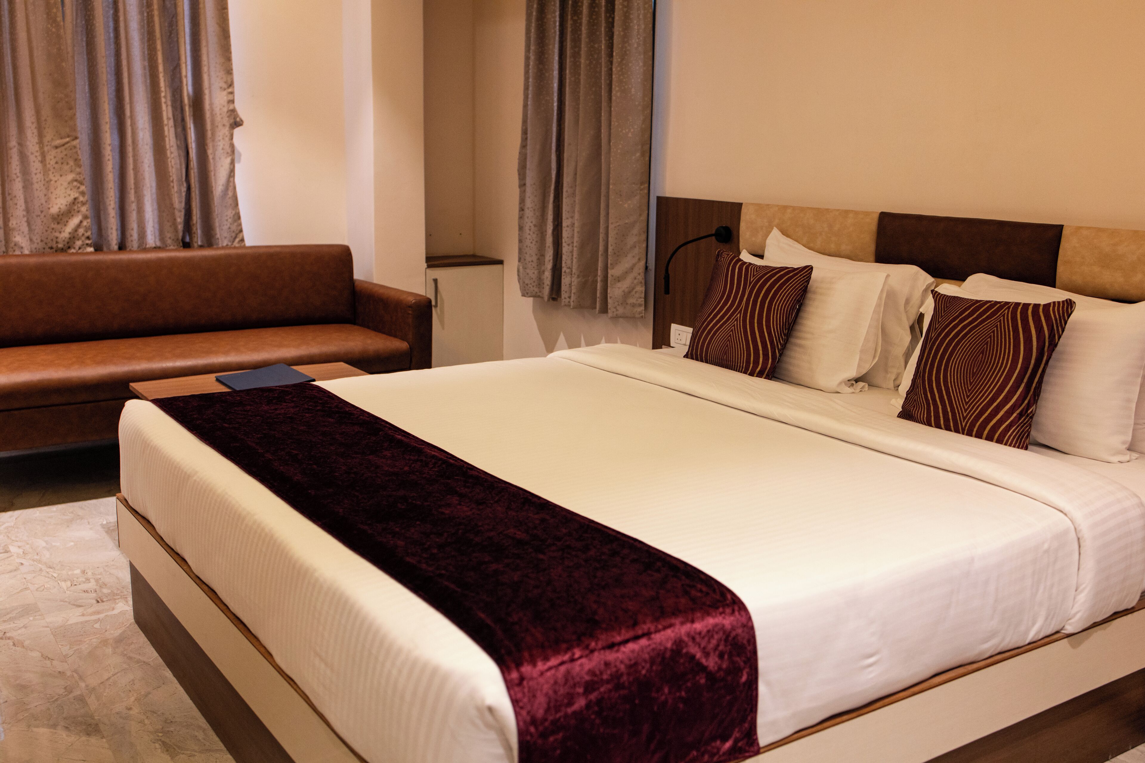 A hotel room with a large bed, a brown sofa, and a small table.