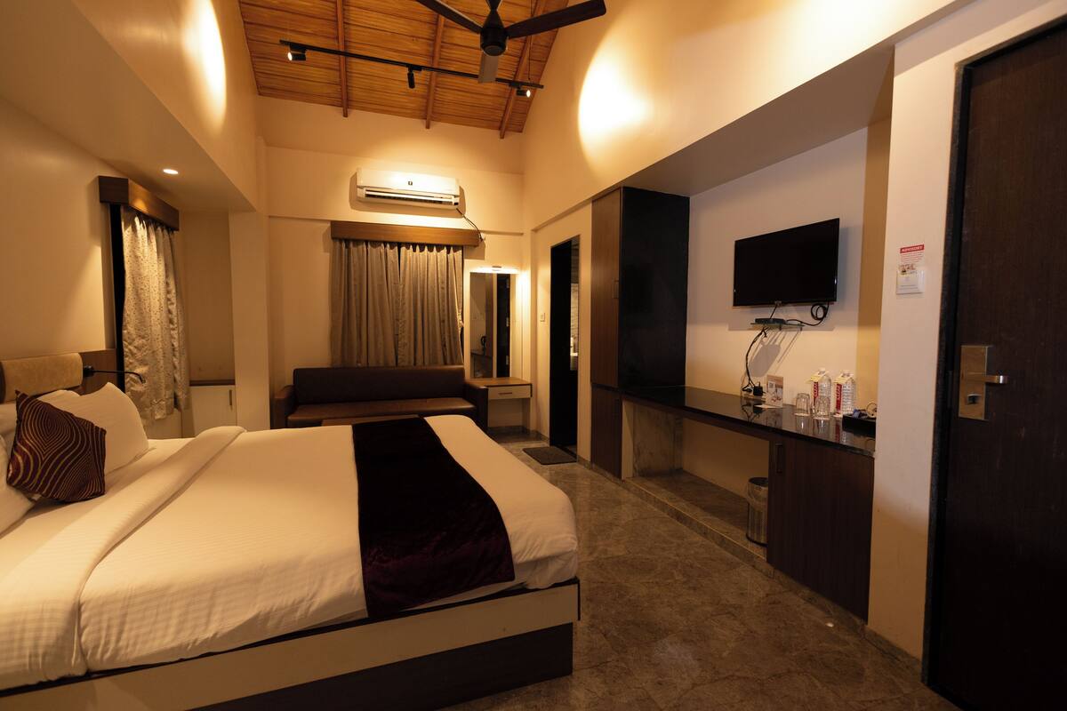 A hotel room with a bed, a desk, a television, and an air conditioning unit.