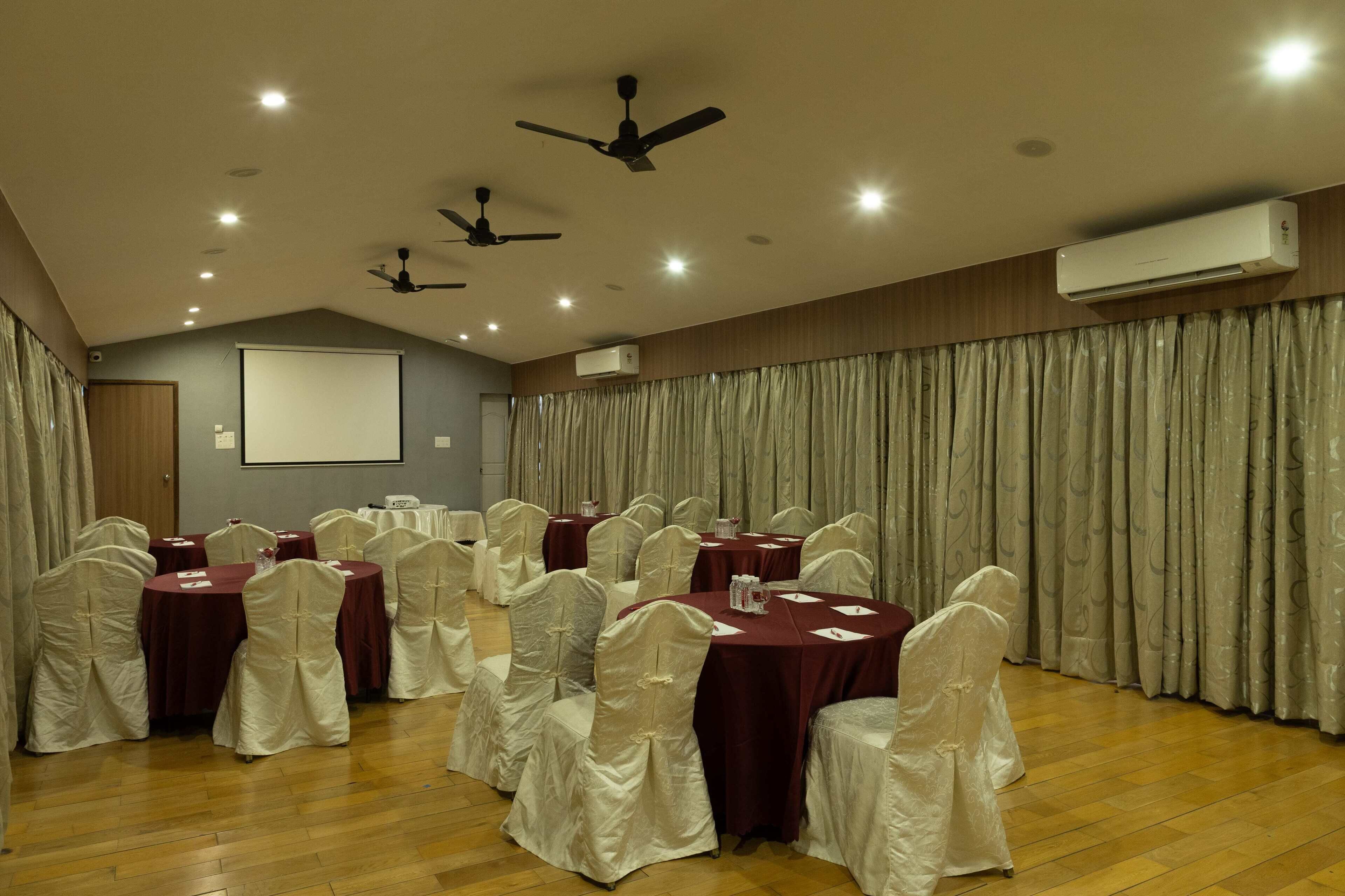 Un salón de conferencias con mesas redondas, sillas blancas y ventiladores de techo.
