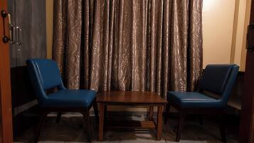 A room with two blue chairs, a wooden table, and a patterned curtain.