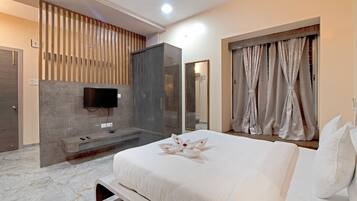 A modern hotel room with a large bed, a TV mounted on the wall, a seating area with a bench, and a shower area.