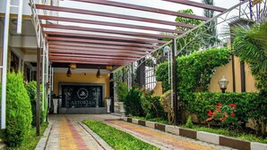 A hotel entrance with a covered walkway, a sign reading "ASTORIAN," and a well-maintained garden with various plants and flowers. - Astorian Grand Hotel (Naivasha)