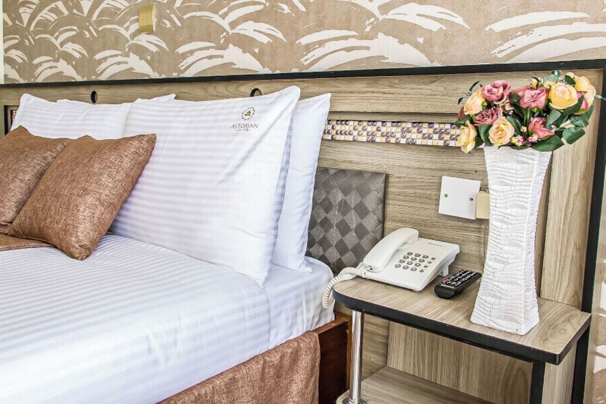 Et hotelværelse med en seng, et natbord med telefon, fjernbetjening og en vase med blomster.