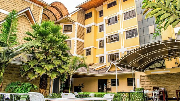 A multi-story building with a yellow facade, multiple windows, and a covered outdoor seating area with chairs and tables. - Astorian Grand Hotel (Naivasha)