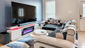 A modern living room with a flat-screen TV, a sofa, and a coffee table. - Modern 6 Bedroom House with Tons of Games, BBQ, 2 85" TVs and Surround Sound! (Houston)