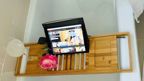 Un tablet su un vassoio di legno in un bagno, con una rosa e un bicchiere d'acqua.