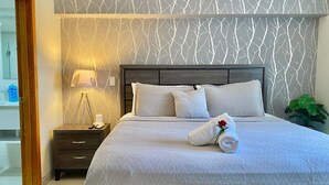 Un lit bien fait, avec une tête de lit à motifs, une lampe de chevet et une table de chevet sur laquelle se trouvent un téléphone et une bouteille.