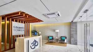 Un espace d’accueil avec une enseigne indiquant « Shanti Tower », un comptoir de réception, deux fauteuils, une lampe de sol et un climatiseur fixé au mur.