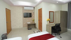 A hotel room with a bed, a desk with a chair, a TV mounted on the wall, and a wardrobe. - Wood Burn Hotel (Bogra)