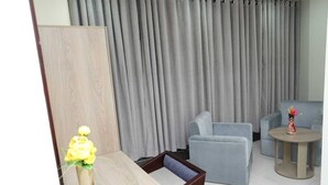 A modern living room with grey curtains, a wooden sideboard, a sofa, a chair, and a small round table with a vase of flowers. - Wood Burn Hotel (Bogra)