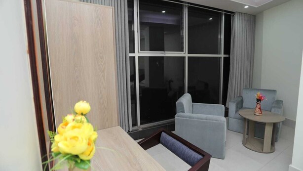 A modern living room with a sofa, a small round table, and a large window with curtains. - Wood Burn Hotel (Bogra)