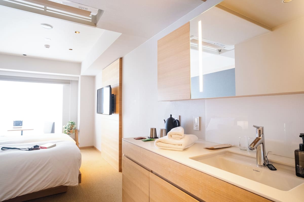 A modern hotel room with a large bed, a bathroom with a double sink, and a TV mounted on the wall.
